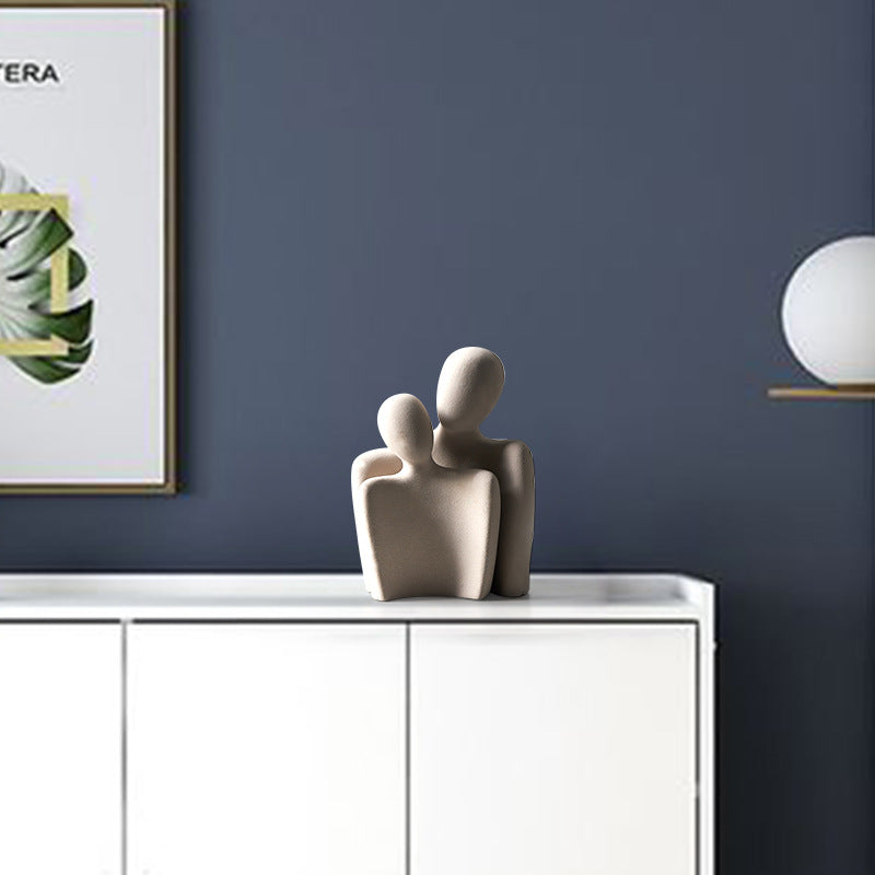 Decorative sculpture of two abstract figures on a white surface with a dark blue wall in the background.