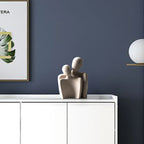 Decorative sculpture of two abstract figures on a white surface with a dark blue wall in the background.