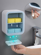 Wall-mounted soap dispenser with soap and sponge compartments in a bathroom setting.