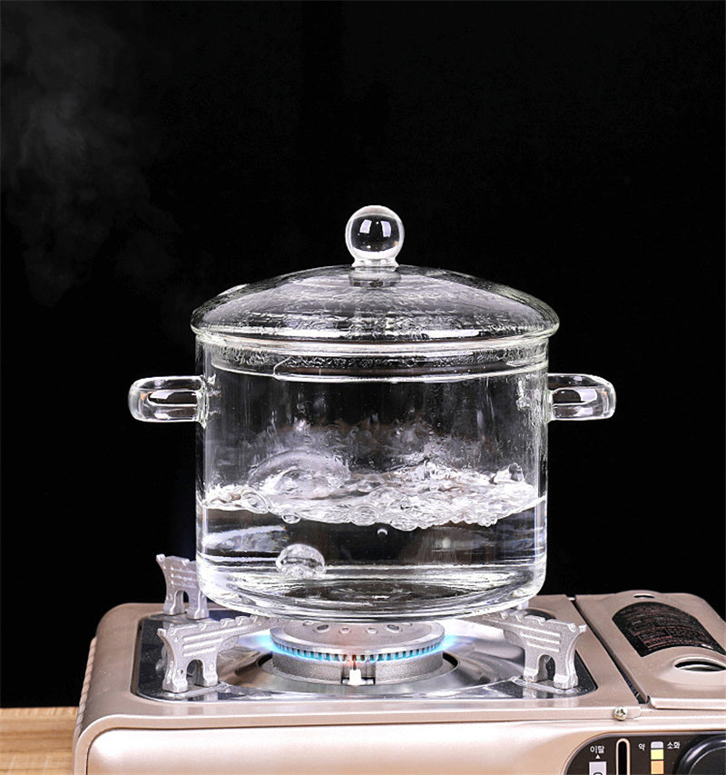 Clear glass pot with a lid on a gas stove against a black background