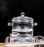 Clear glass pot with a lid on a gas stove against a black background