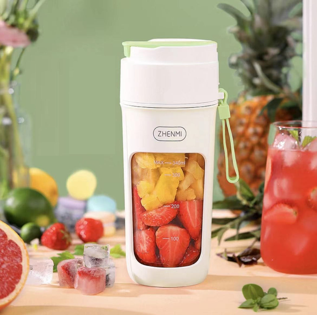 White Zhenmi fruit juice maker with fruits inside, surrounded by fresh fruits and a drink on a wooden surface.
