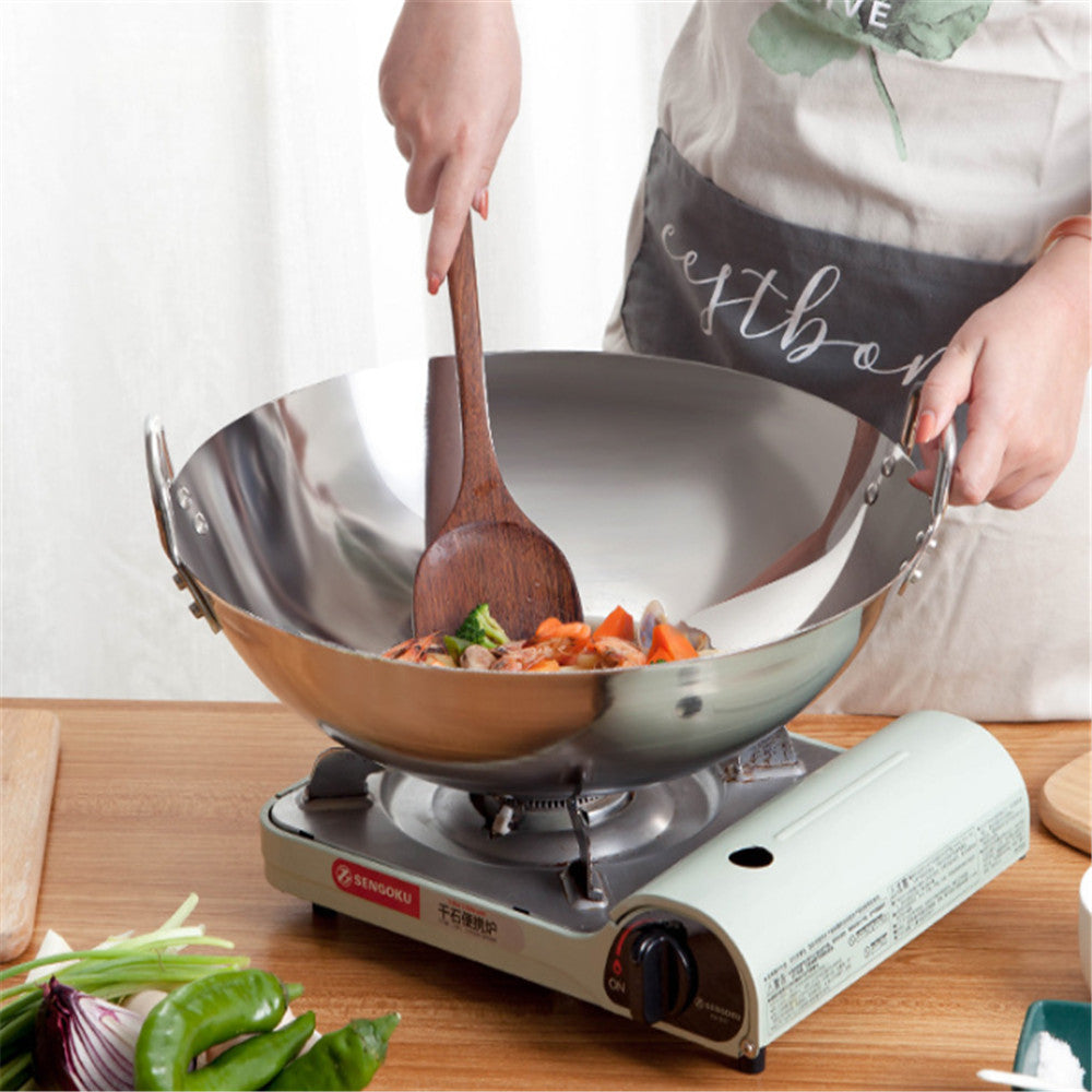 Person cooking in a wok on a portable stove with a wooden spoon