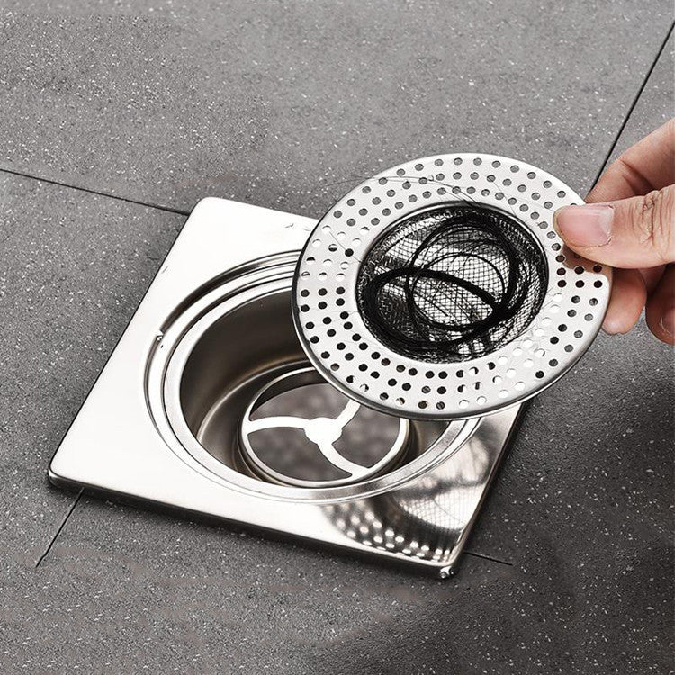 Hand holding a metal drain cover over a sink drain on a gray floor.
