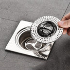 Hand holding a metal drain cover over a sink drain on a gray floor.