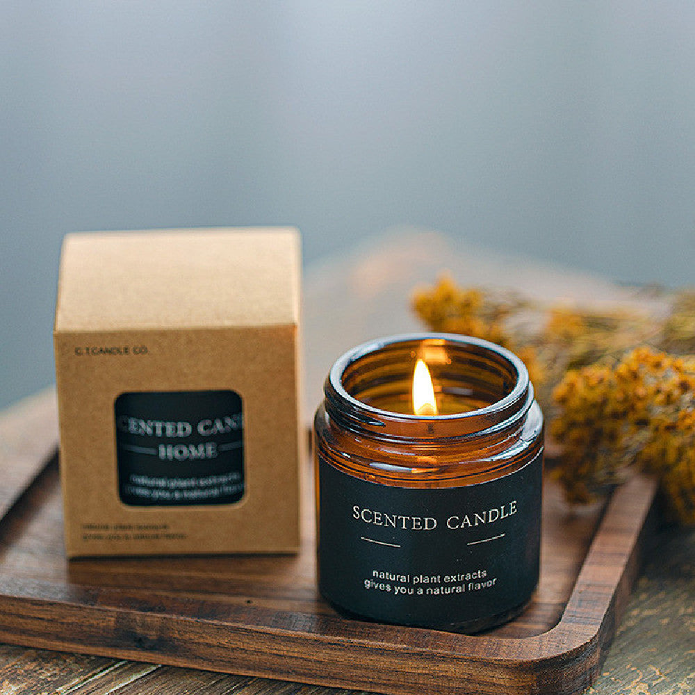 Scented candle with a lit flame next to its packaging on a wooden surface.